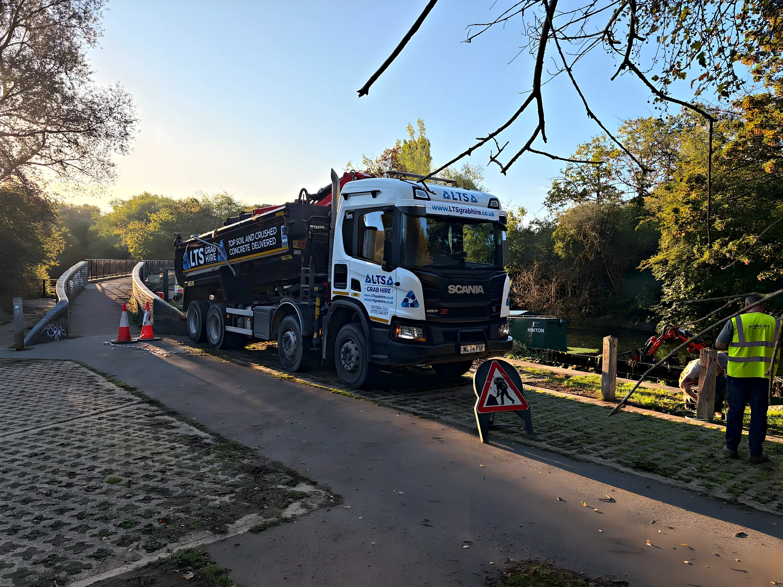 An eight-wheel Scania grab lorry parked on a towpath in autumn sunshine