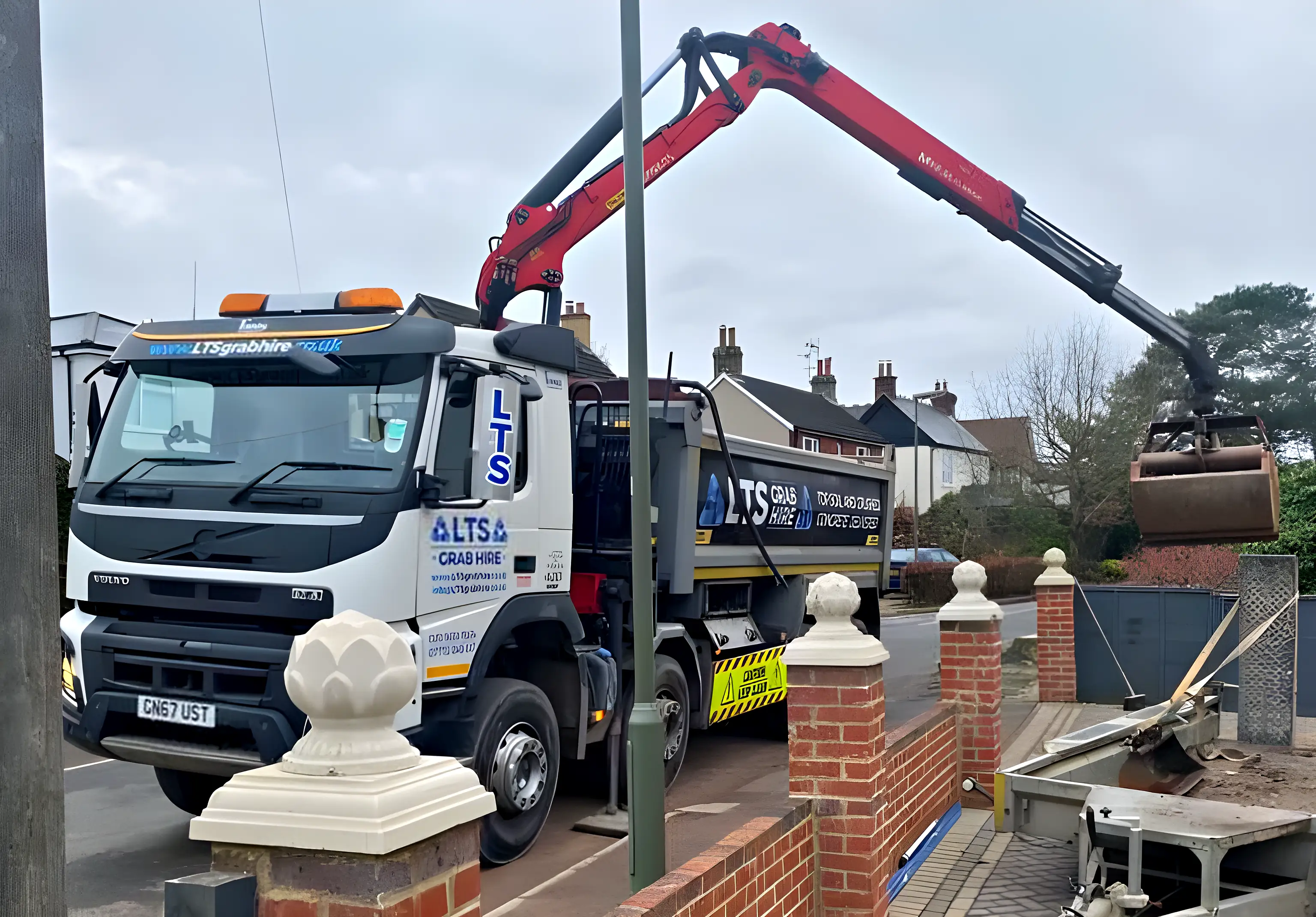 A grab arm lifting soil over a garden wall from the road