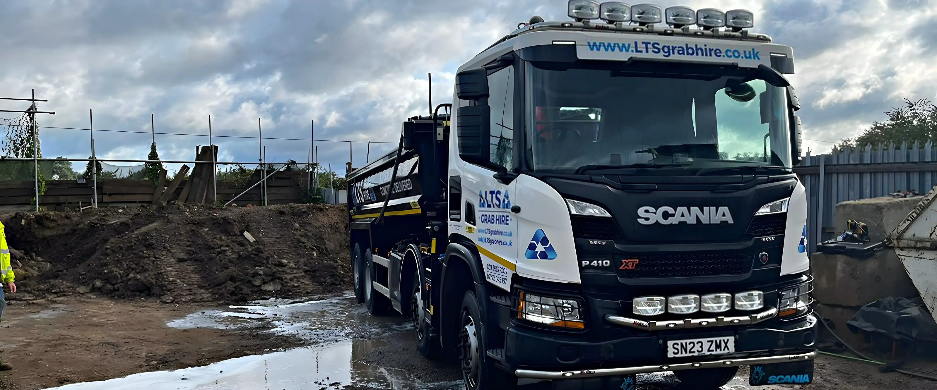 A grab lorry on a cleared building site with an excavator behind it