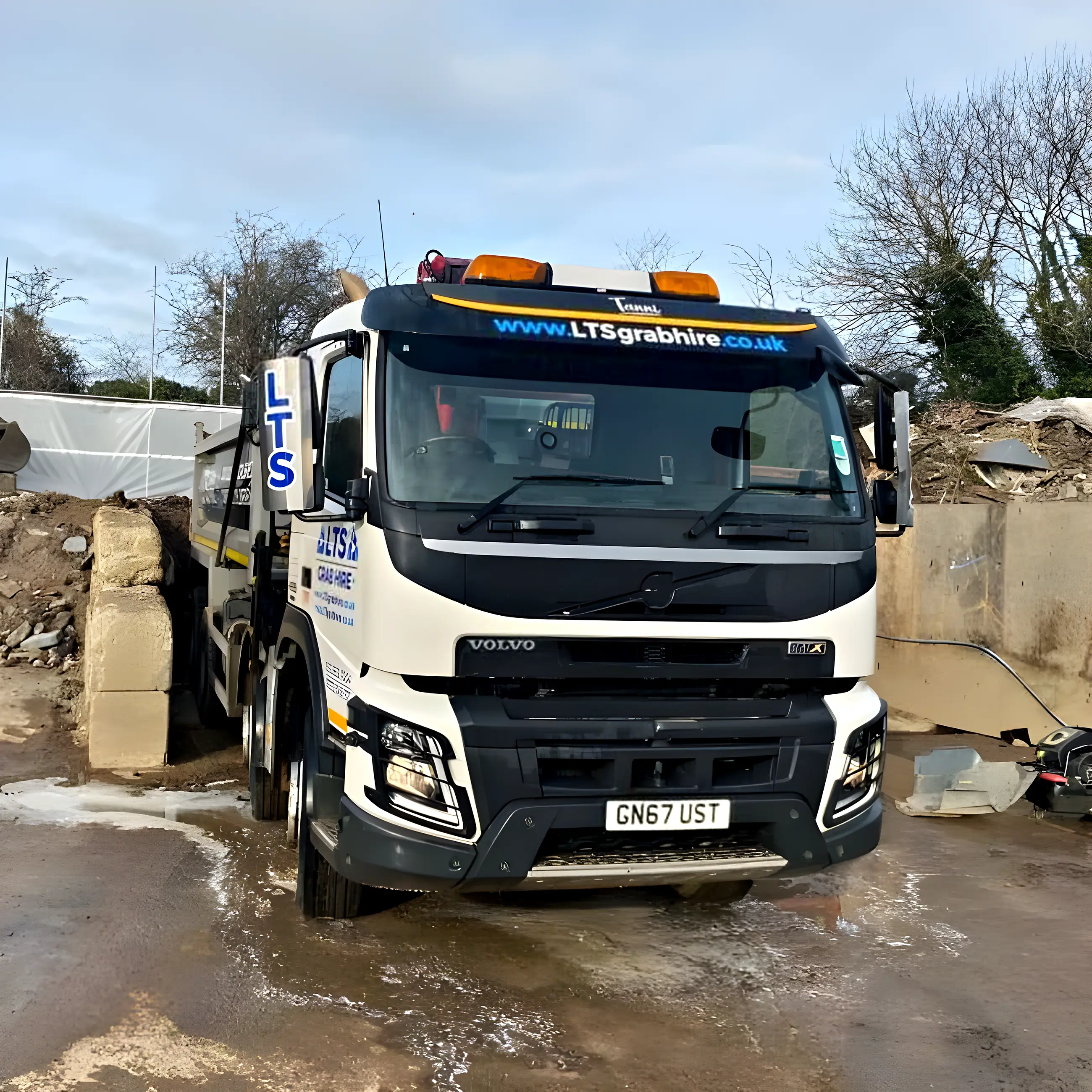 An eight-wheel grab lorry head on at the yard beside the timber piles
