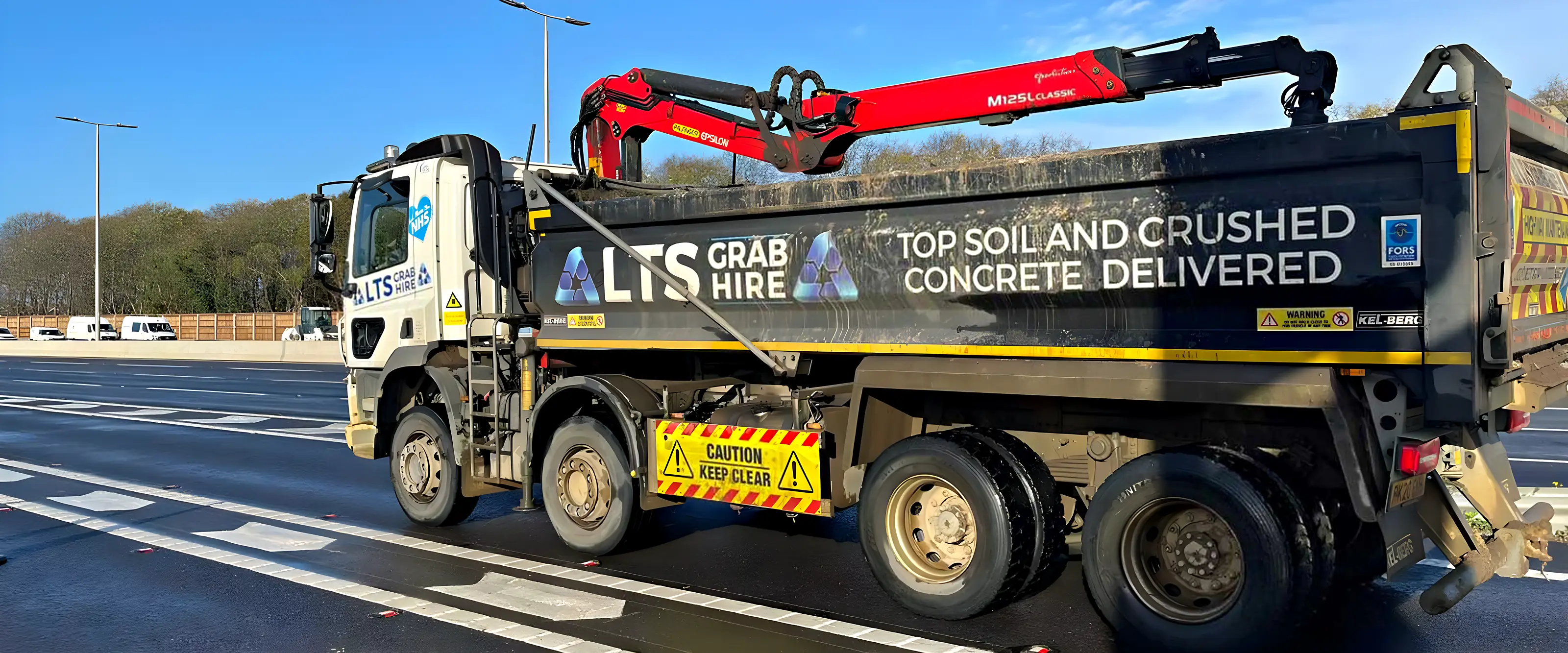A grab lorry with a yellow-lined body on a new road under a clear blue sky