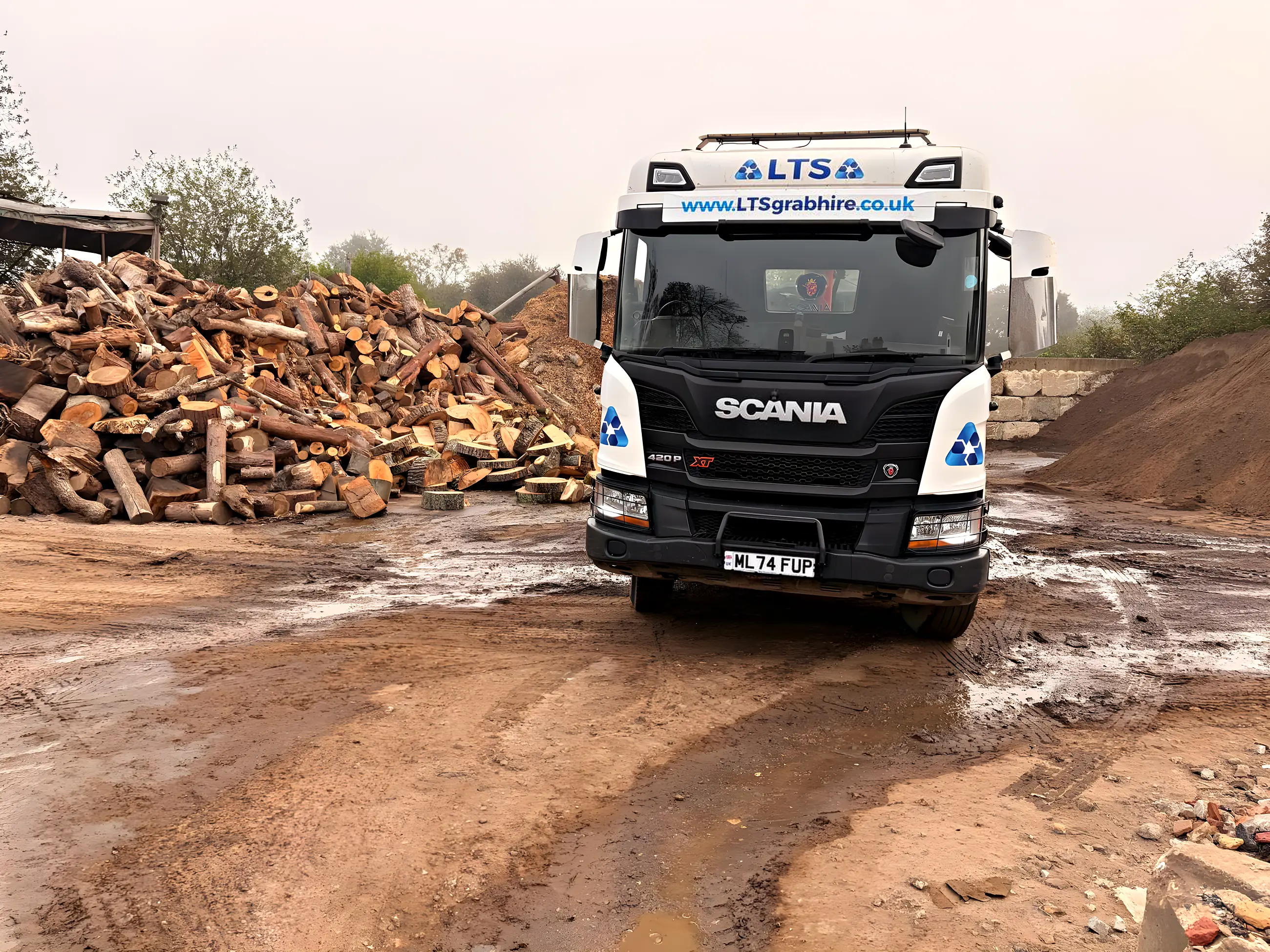 An eight-wheel grab lorry head on at the yard beside the timber piles