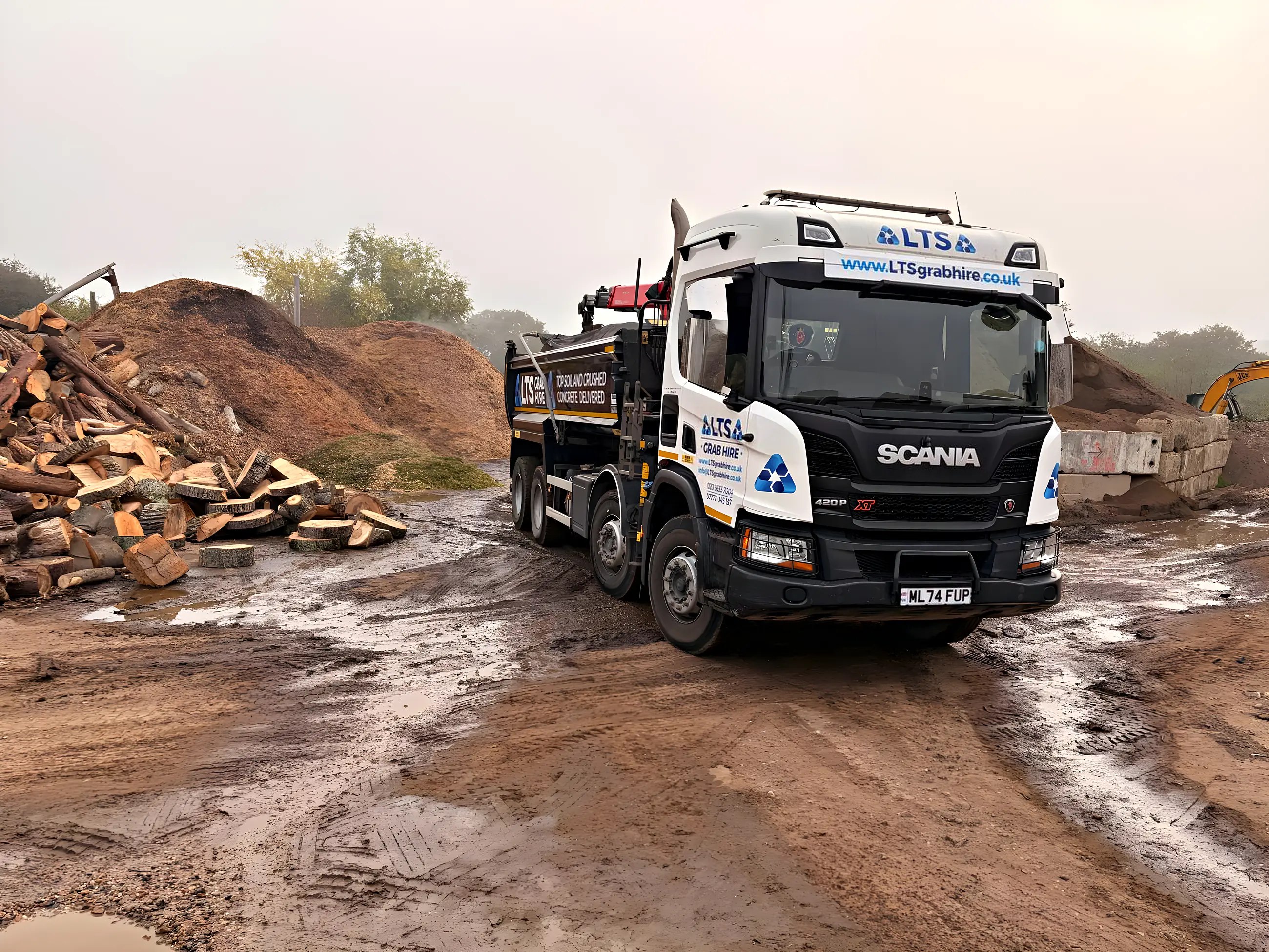 An eight-wheel grab lorry at the yard beside the soil and timber piles